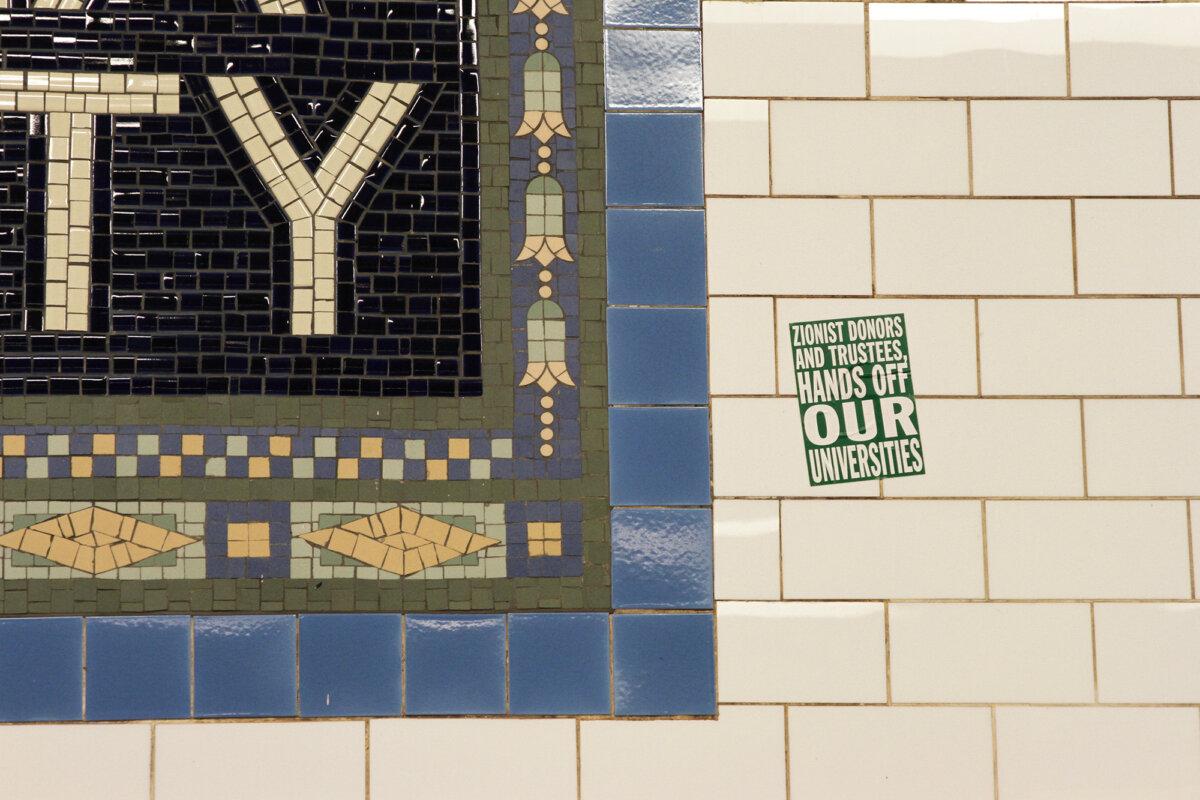 A sticker on the wall of the Columbia University subway station at 116th Street tells Zionists to keep their hands off universities. Photo taken on April 23, 2024. (Richard Moore/The Epoch Times)