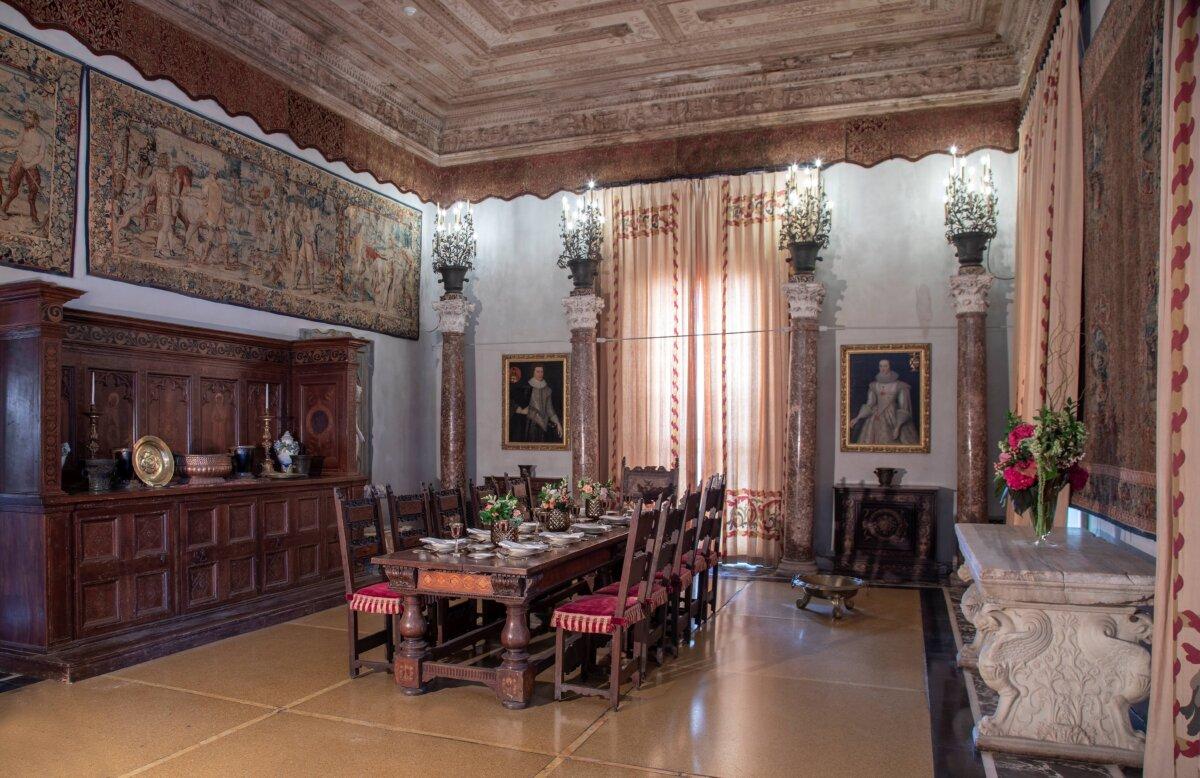 The main dining room on the first floor conveys medieval and Renaissance aesthetics. The walls are covered with original 16th-century Belgium tapestries, with a main rectangular tapestry featuring the Roman god Mercury, and images of merchants, travelers, and transporters of goods. The ceiling is carved and stained wood and is set off by a late 17th-century wall-hung valance of velvet with embroidery in silver and gold metallic bullion threads with compatible bullion fringe. The window wall features four acanthus leaf-topped marble Corinthian columns that carry upright chandeliers featuring orange tree designs. (Robin Hill/Vizcaya Museum and Gardens) <span style="color: #ff0000;"> </span>