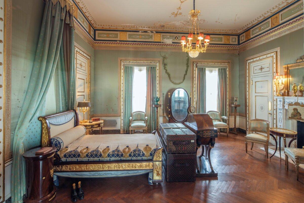 The master bedroom has an Italian neoclassical gilt, bronze-mounted bed with a tasseled canopy backdrop. The walls are painted in rococo green; the plaster ceiling has a raised design in gold on cream/white with a ceiling border displaying gold and green framed segments of repeating motifs. Raised plaster designs complementing ceiling moldings are repeated around doors and windows and feature rosettes and stars. The floor is wood parquet in a herringbone pattern. (Robin Hill/Vizcaya Museum and Gardens)