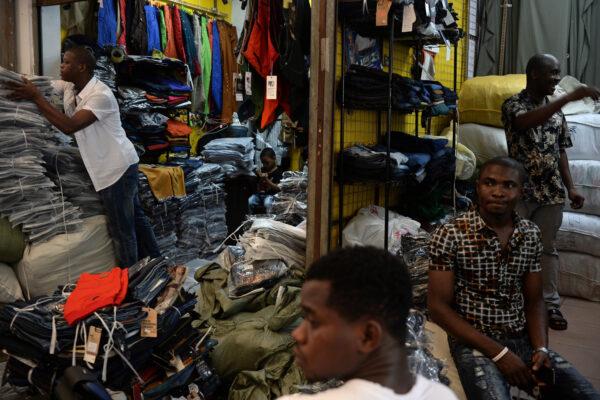 Lamine Ibrahim (L) from Guinea works as his four-year-old son (back C) looks on at their shop inside a clothing wholesale market in Guangzhou, China on August 26, 2013. (STR/AFP via Getty Images)
