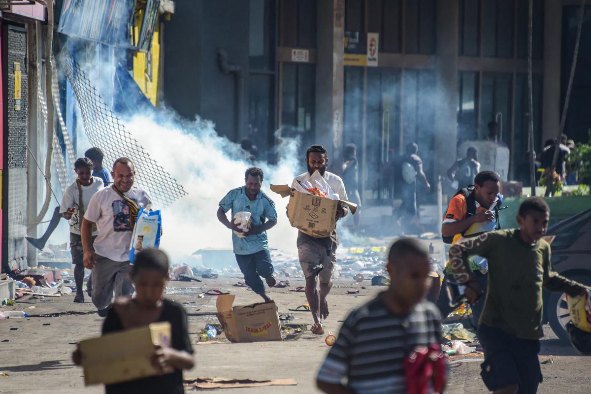 People run with merchandise as crowds leave shops with looted goods amid a state of unrest in Port Moresby on Jan.10, 2024. (Andrew Kutan/AFP via Getty Images)