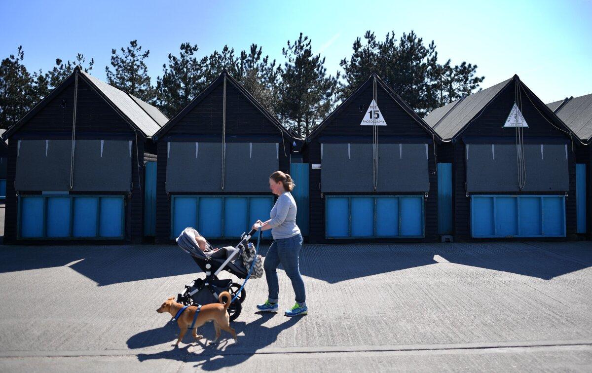 A woman pushes a baby buggy as she walks a dog past closed-down stalls at an empty Harbour Market, during lockdown, in Whitstable, southeast England, on April 11, 2020. (Ben Stansall/AFP via Getty Images)