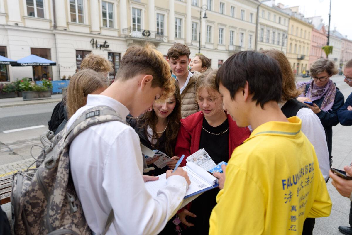 Passersby sign a petition held by a Falun Dafa practitioner during a march through the center of Warsaw, Poland, on Sept. 9, 2022. (Mihut Savu/The Epoch Times)