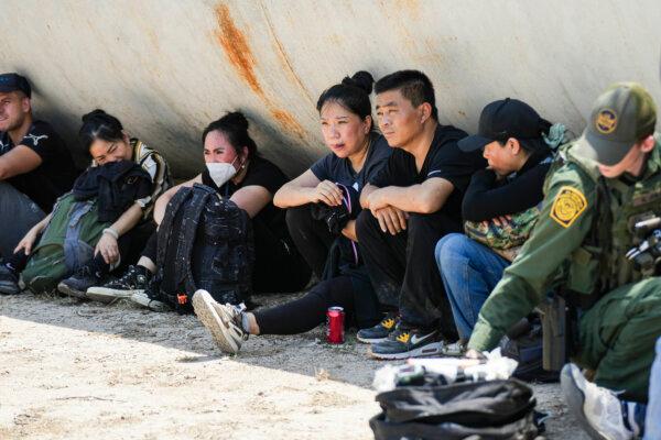 Chinese illegal immigrants wait while a Border Patrol agents provides medical care to a woman within a large group of illegal immigrants near Eagle Pass, Texas, on May 20, 2022. (Charlotte Cuthbertson/The Epoch Times)
