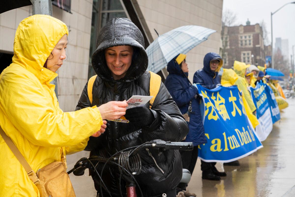 A Falun Gong practitioner hands a pedestrian a flyer about the persecution of Falun Gong in China, during an event in front of the Chinese Consulate in Toronto on April 25, 2026, to commemorate the 27th anniversary of Falun Gong practitioners' April 25, 1999, appeal in Beijing calling for freedom of belief. (Evan Ning/The Epoch Times)