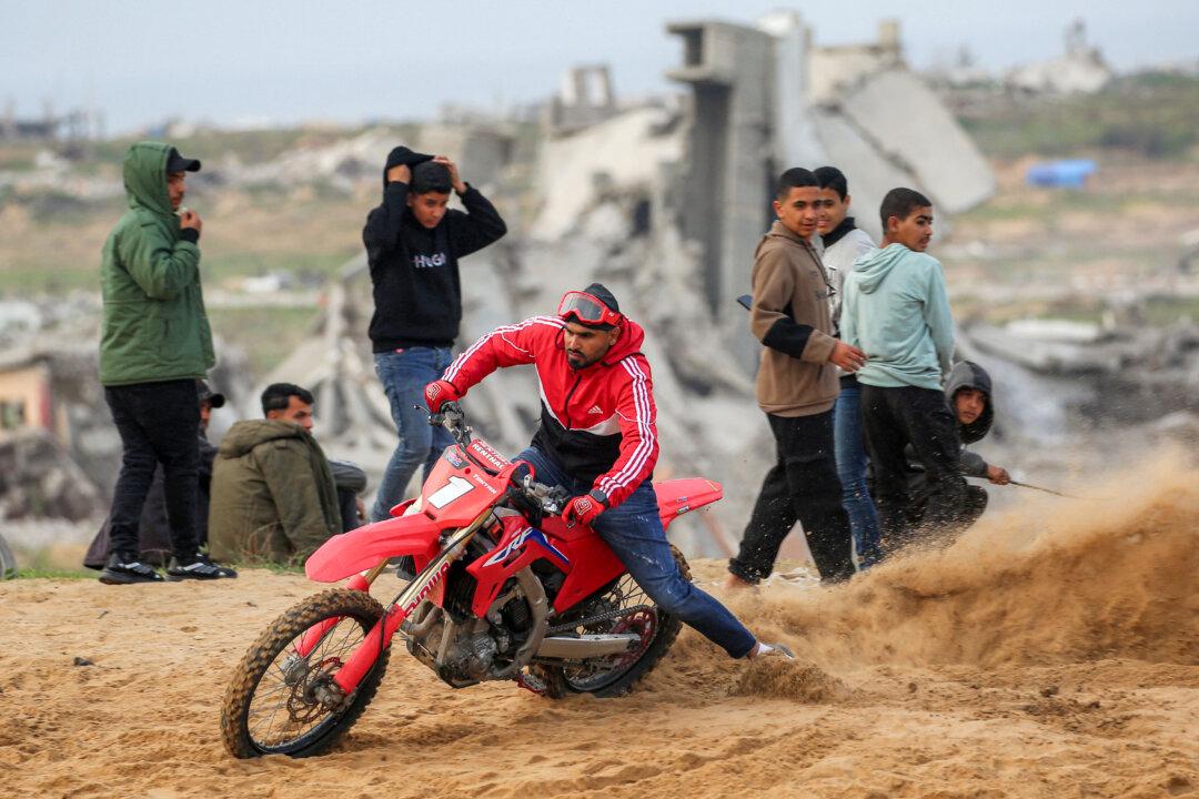 TOPSHOT - A man performs stunts with a dirt bike on sand dunes near destroyed buildings in the Zahra neighbourhood, southwest of Nuseirat in the central Gaza Strip, on February 6, 2026. Since October 10, a fragile US-sponsored truce in Gaza has largely halted the fighting between Israeli forces and Hamas, but both sides have alleged frequent violations. (Photo by Eyad Baba / AFP via Getty Images)