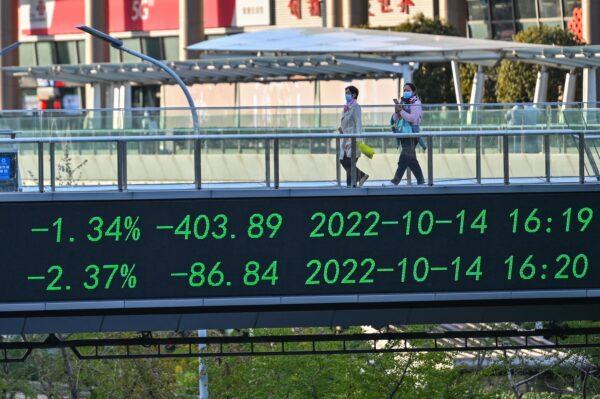 People walk across a bridge with a stocks indicator board in the financial district of Lujiazui in Shanghai, on Oct. 17, 2022. (Hector Retamal/AFP via Getty Images)