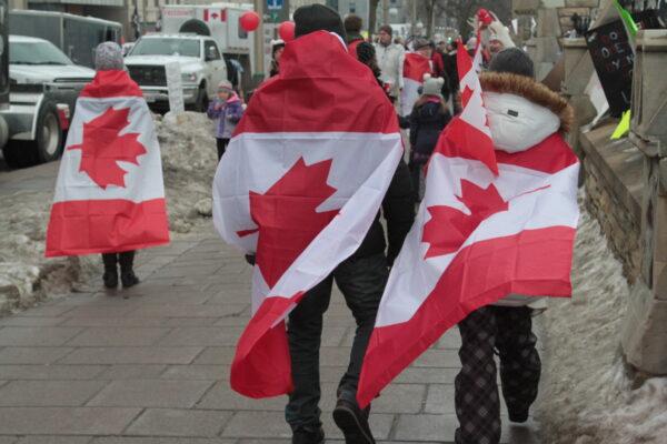 Protesters draped in Canadian flags walk at the site of the truck protest in Ottawa on Feb. 12, 2022. (Richard Moore/The Epoch Times)