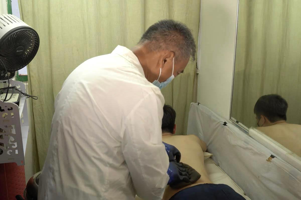Tse See-li treating his patient for blood stasis by stacking a hot herbal medicinal pack on the painful area, in this still taken from the video series "A Hundred Diseases and a Hundred Medicines." (Screenshot via YouTube/GreenEastern)