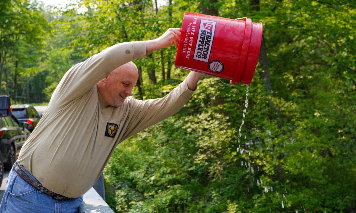 Mike Torelli empties a bucket of trout into the Neversink River in Cuddebackville, N.Y., on May 23, 2023. (Cara Ding/The Epoch Times)