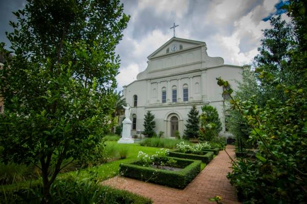 The rear view of St. Louis Cathedral provides a glimpse into what is called St. Anthony’s Garden, which features a marble statue of the Sacred Heart of Jesus. Although much less elaborate than its front, the back view of the cathedral also conveys the balanced architectural elements of columns and arches, with an exterior clock—similar to the one over the cathedral’s entryway—offered to visitors of the garden as well. (Courtesy of the Archdiocese of New Orleans)