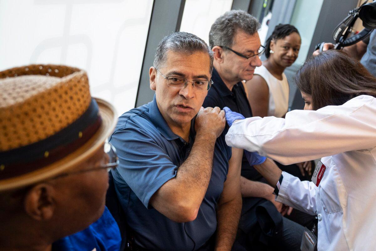 U.S. Health Secretary Xavier Becerra (C), with Pfizer CEO Albert Bourla to his left, receives one of the new COVID-19 vaccines at a CVS in Washington on Sept. 20, 2023. (Drew Angerer/Getty Images)