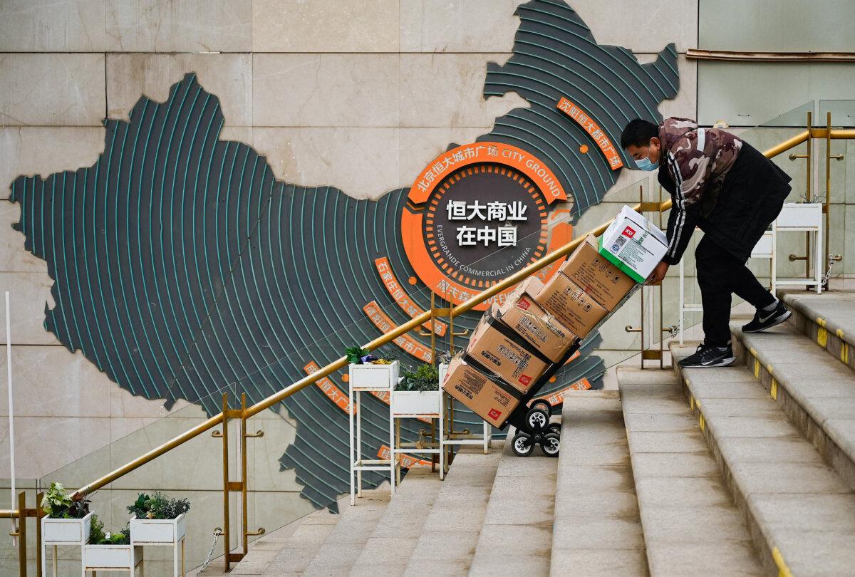 A worker pushes a cart in front of a sign showing Evergrande Group's China operation at a housing complex by the property developer in Beijing on Dec. 8, 2021. (Noel Celis/AFP via Getty Images)