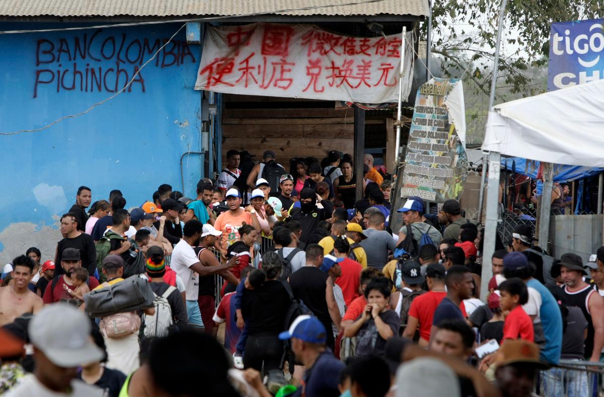 Migrants line up for immigration processing as merchants offer services in both Spanish and Chinese in Lajas Blancas, Panama, on Feb. 17, 2024. (Bobby Sanchez for The Epoch Times)