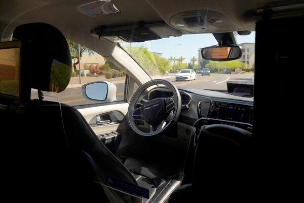 A Waymo minivan moves along a city street as an empty driver's seat and a moving steering wheel drive passengers during an autonomous vehicle rid, in Chandler, Ariz., on April 7, 2021. (Ross D. Franklin/AP Photo)
