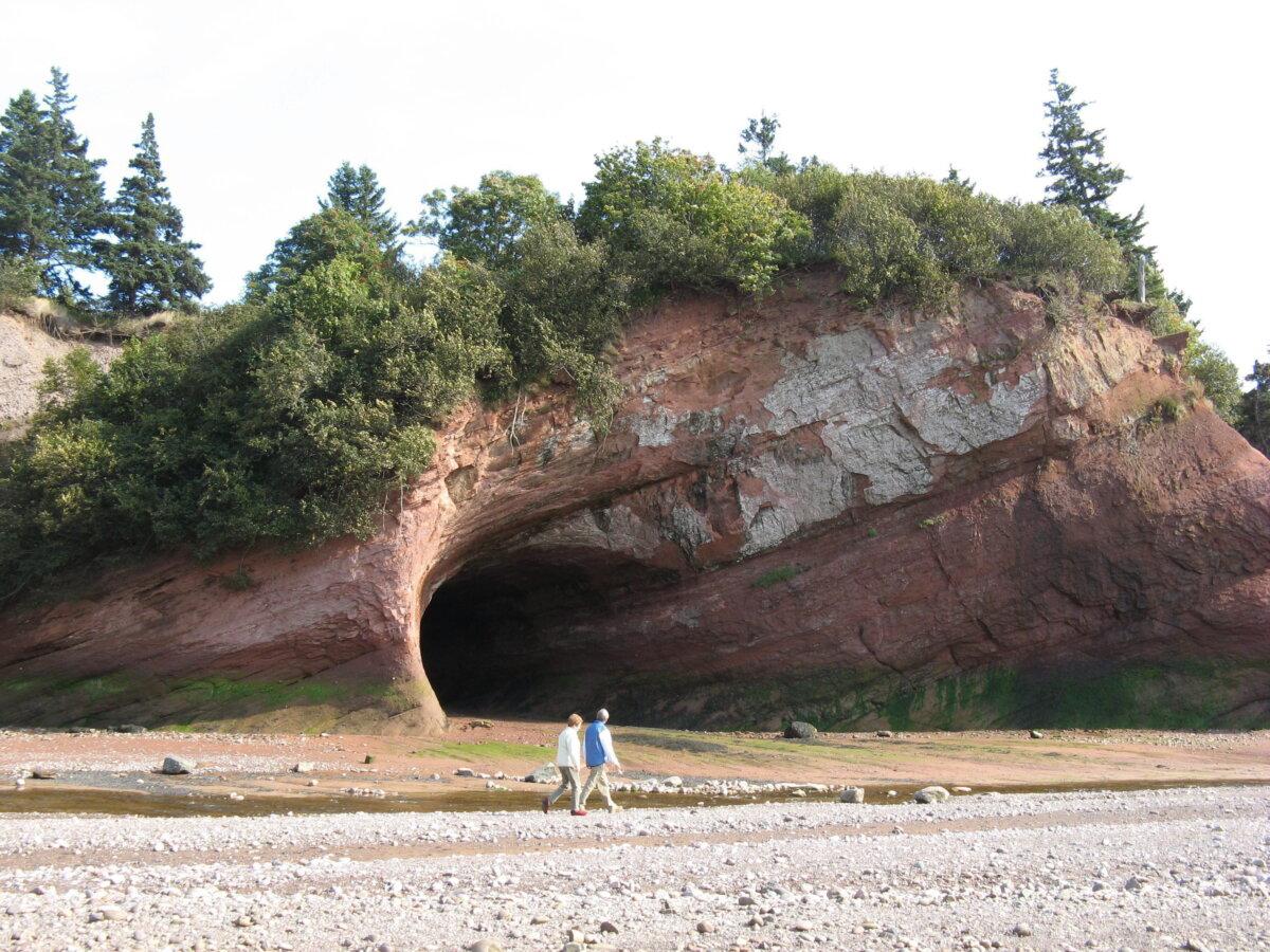 A couple walks on the ocean floor at low tide to view the caves carved in the red sandstone by the Bay of Fundy, N.B., in this undated photo. (The Canadian Press/Kevin Bissett)