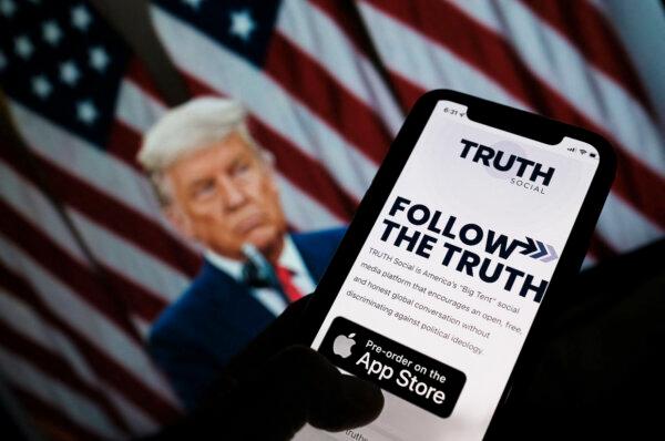 This illustration photo shows a person checking the app store on a smartphone for Truth Social with a photo of former President Donald Trump on a computer screen in the background in Los Angeles on Oct. 20, 2021. (Chris Delmas/AFP via Getty Images)