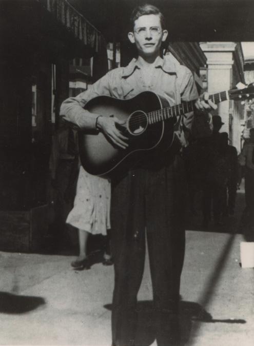 Hank Williams playing guitar on a sidewalk in Montgomery Alabama, 1938. Alabama Department of Archives and History. (Public Domain)