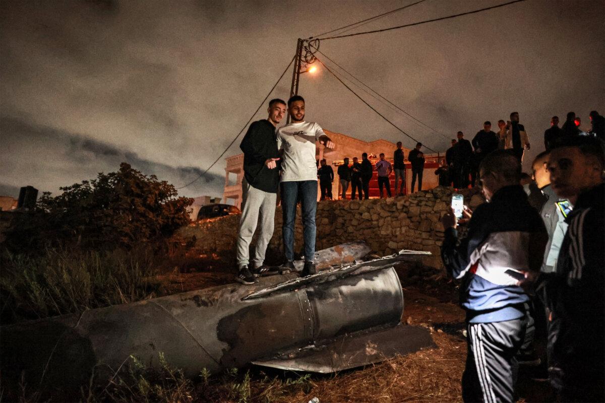 Palestinian youths pose for a picture atop a fallen projectile in the West Bank after Iran launched a barrage of missiles at Israel on Oct. 1, 2024. (Zain Jaafar/AFP via Getty Images)
