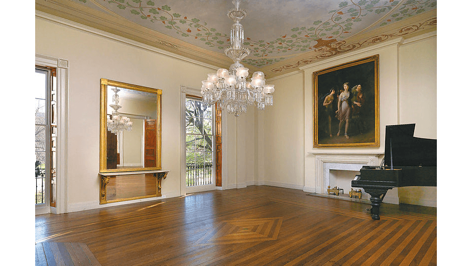 The second-floor parlor’s diamond design inset in the parquet floor aligns perfectly with the contrasting glass-light and crystal chandelier overhead. The parlor’s painted 15-foot-high ceiling features motifs of ivy and grapevine overflowing from urns. Floor-to-almost-ceiling windows allow light to flood the room. The room’s gilded mirror is uniquely accented with gilded corbels topped with a marble slab, which serves as an accent tabletop. (Photography by Bruce White)