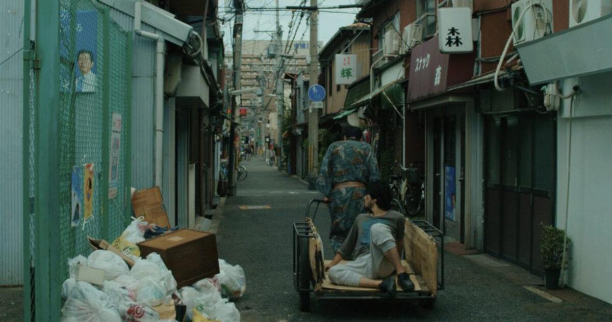 Tsuchiro (Takahiro Fujita) supports Tatsumi (Yuwa Kitagaki, seated) in his grief, in “A Dobugawa Dream.”  (GJW+)