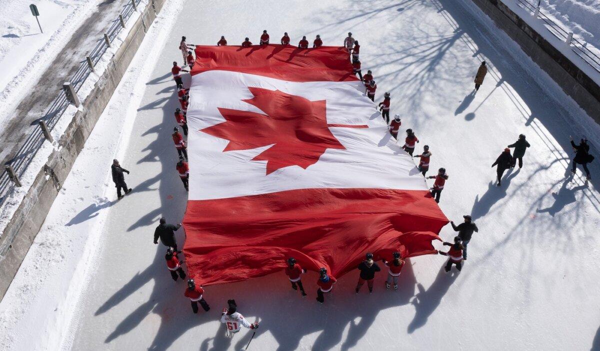 Local youth skate with a large Canadian flag on the Rideau Canal to launch celebrations marking National Flag of Canada Day in Ottawa on Feb. 14, 2025. (The Canadian Press/Adrian Wyld)