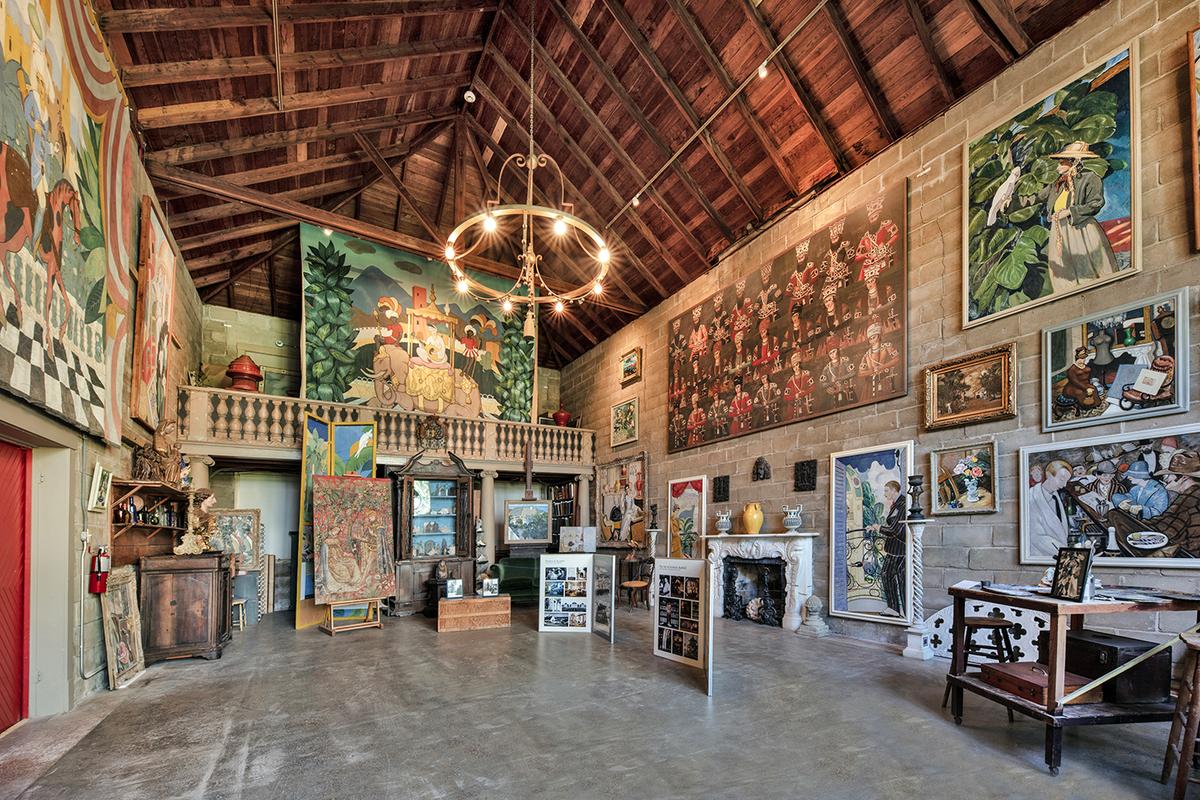 The art studio has a vaulted cypress wood ceiling, gray terrazzo floor, and a simplistic metal chandelier. It is a multicolored palette of assorted large landscapes and portraits in saturated hues, painted primarily by Bonnet House’s founder. They are hung against unpainted cinder block walls. Additionally, Bartlett painted the trompe-l’oeil balustrade at the back of the room. (J Christopher Gernert/Courtesy of Bonnet House)
