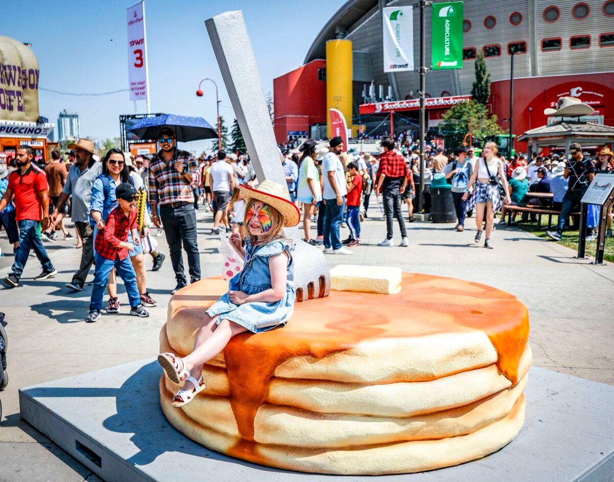A young girl sits on a stack of pancakes for the hundredth anniversary of the Stampede pancake breakfast on Family Day at the Calgary Stampede parade in Calgary, on July 9, 2023. (The Canadian Press/Jeff McIntosh)