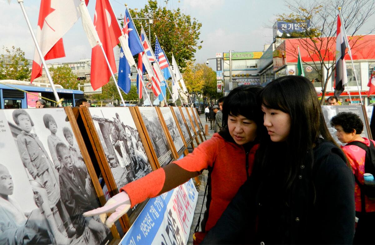 A mother shows her daughter photos of the horrors of the Korean War, which began June 25, 1950, at the Korean War Photo Exhibition in downtown Seoul, South Korea, on Nov. 12, 2011. (Courtesy of Ahn Jae-chul, president of The World Peace Freedom United)