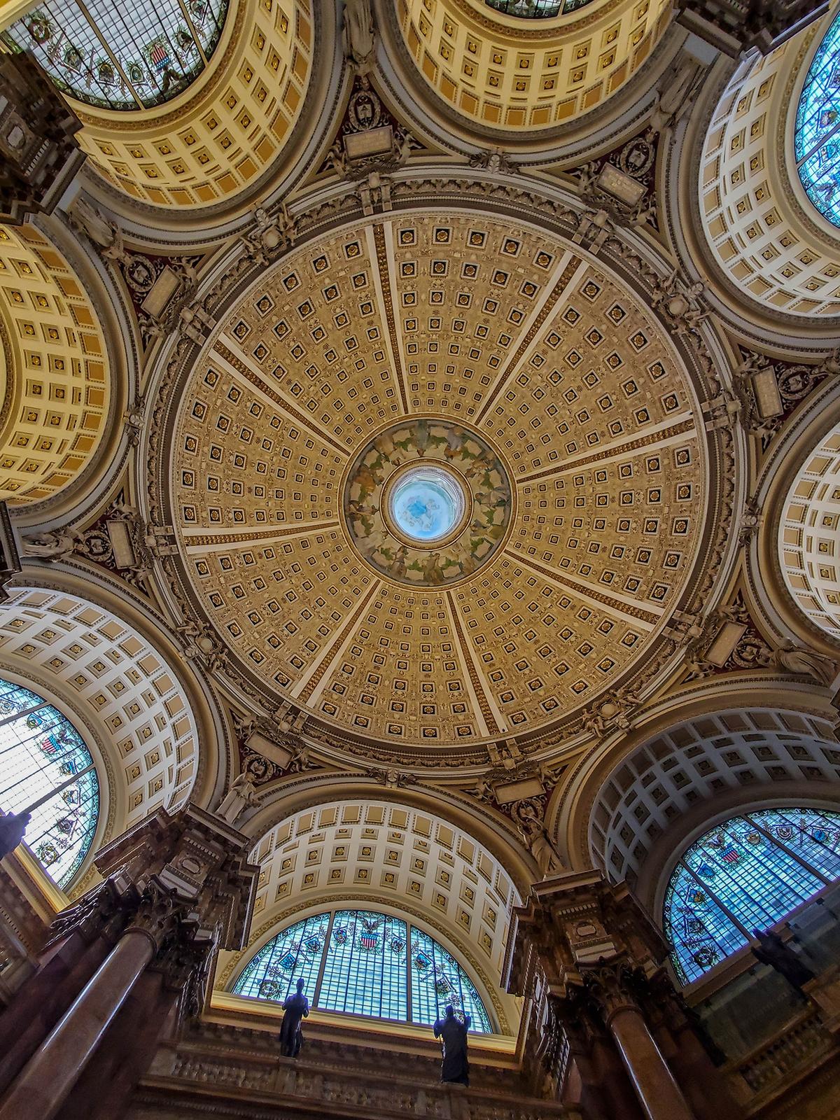 The Main Reading Room's coffered dome, 160 feet above the floor, is resplendent with 320 framed and gilded rosettes. These surround an elaborate painting, titled “<a href="https://blogs.loc.gov/loc/2024/06/look-up-its-blashfields-mural/" target="_blank" rel="nofollow noopener">Human Understanding</a>,” by American painter and muralist Edwin Howland Blashfield (1848–1936). At the center of Blashfield's painting is a female figure. Set against a soft blue background, she is surrounded by 12 painted figures representing various regions of the world, which were thought to be contributors to Western civilization. Extravagant cornice-topped arches, as well as massive arches decorated with numerous rosettes, coordinate with the ones in the main dome. (ChicagoPhotographer/Shutterstock)
