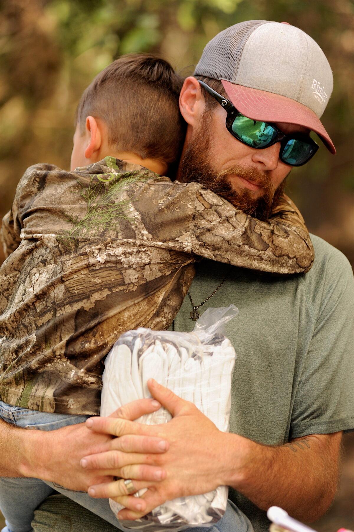 Zachary Clark holds his 5-year-old son while describing the catastrophic flooding along the Guadalupe River near Comfort, Texas, on July 7, 2025. (Neil Hernandez for The Epoch Times)