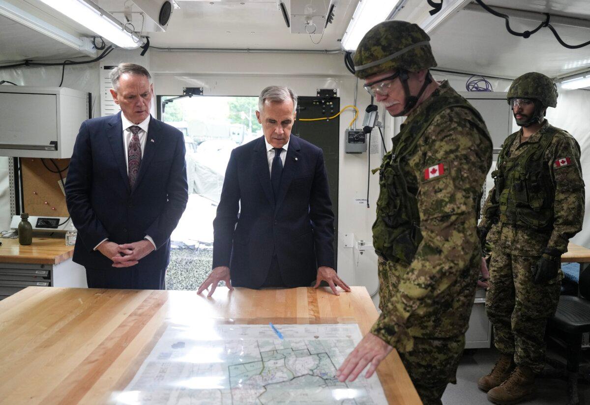 National Defence Minister David McGuinty and Prime Minister Mark Carney talk with Captain Michael Rankin of 32 Signal Regiment, during a visit to a command post at Fort York Armoury in Toronto on June 9, 2025. (The Canadian Press/Chris Young)
