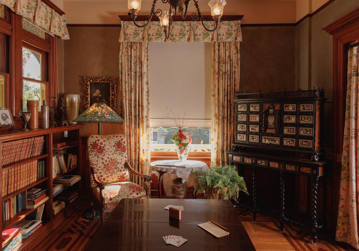 With its intricate Spanish chest and wood parquet-patterned floor, the first-floor library was the Kimberlys' favorite room. A stained-glass floor lamp, a patterned fabric chair, and window treatments bring color to the room. Additionally, the lavish brass Victorian lighting fixture adds interest with its ruffled-edge etched glass shades. (Ryan Schude/Kimberly Crest House & Gardens)