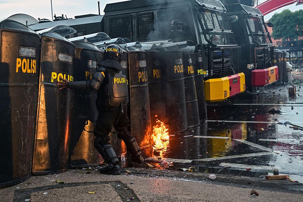 A policeman reacts as a 'Molotov cocktail' burns on the ground during a protest against the Mobile Brigade Corps or 'Brimob,' after the death of a motorbike taxi driver on Aug. 28, in front of the governor's residence in Surabaya on Aug. 29, 2025. (JUNI KRISWANTO/AFP via Getty Images)