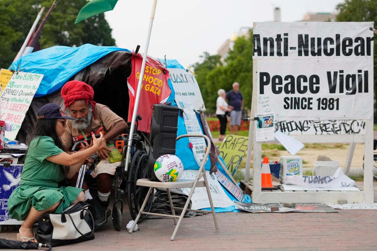 Philipos Melaku-Bello (2nd L) looks over a passerby's phone while at the White House Peace Vigil in Lafayette Park across the street from the White House in Washington, on Sept. 5, 2025. (Pablo Martinez Monsivais/AP Photo)