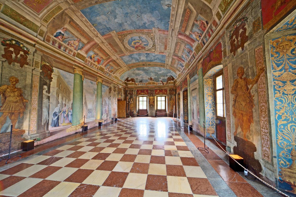 The Ceremony Hall is the heart of the palace and features 17th-century frescoes painted by Florentine priest and artist Donato Arsenio Mascagni. The artist's use of perspective makes the room appear larger than it is. Mascagni depicted scenes of Florence and Venice on the long walls with personifications of the virtues featured above on the painted balustrade. (<a href="https://commons.wikimedia.org/wiki/File:Hellbrunn_banqueting_hall_01.jpg" target="_blank" rel="nofollow noopener">MatthiasKabel</a>/<a href="https://creativecommons.org/licenses/by-sa/3.0/deed.en" target="_blank" rel="nofollow noopener">CC BY-SA 3.0</a>)
