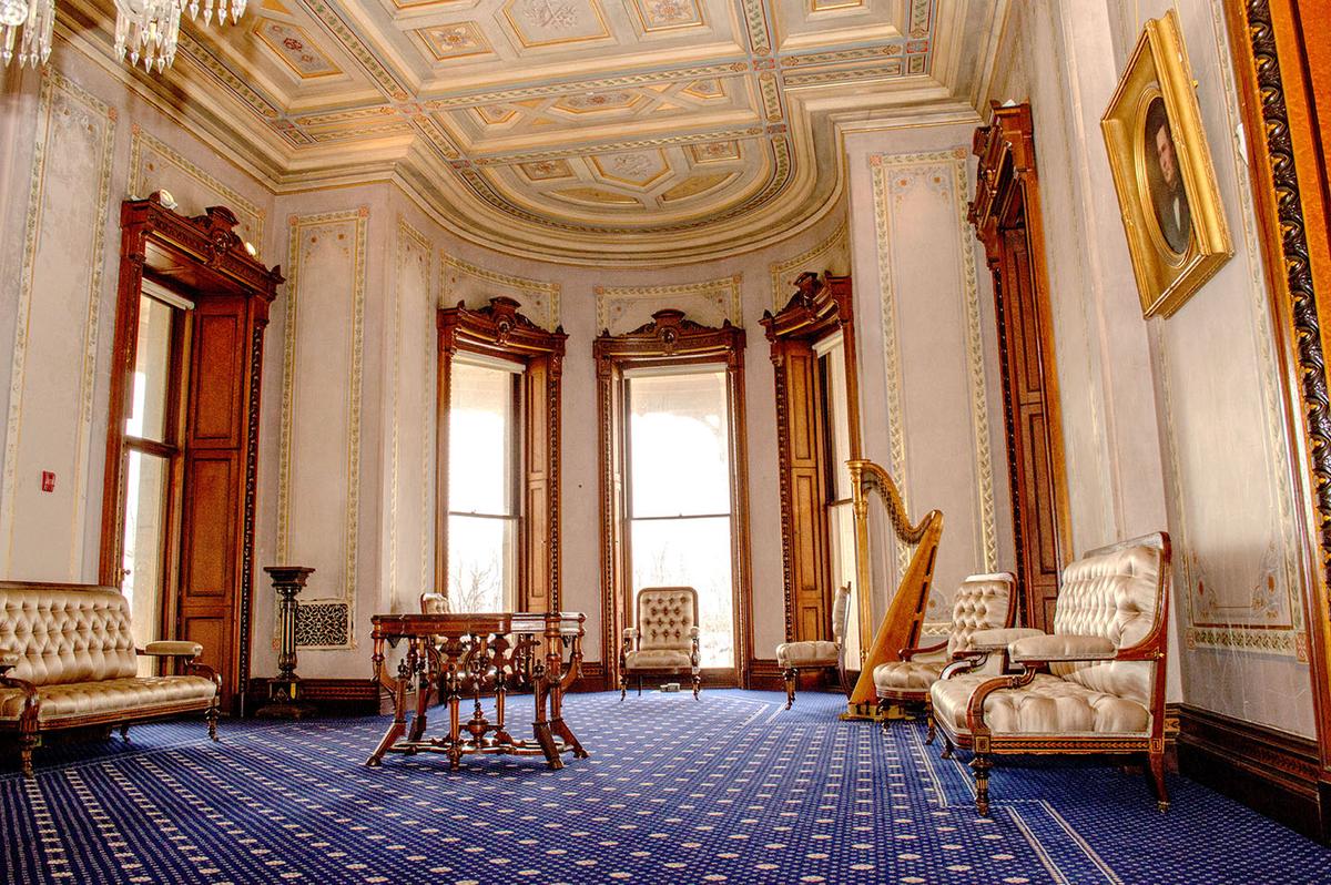 Despite the music room’s featured 19th-century harp, the room’s name originated from its decorative designs: Instruments are painted in the original 1868 paneled ceiling and inlaid in boxwood in the pocket doors. The current carpet was installed by Paramount Studios for the 2004 film “The Stepford Wives,” starring Nicole Kidman and Matthew Broderick. (<a href="https://www.sarahgroteart.com/" target="_blank" rel="nofollow noopener">Sarah Grote Photography</a>/Lockwood-Mathews Mansion Museum)