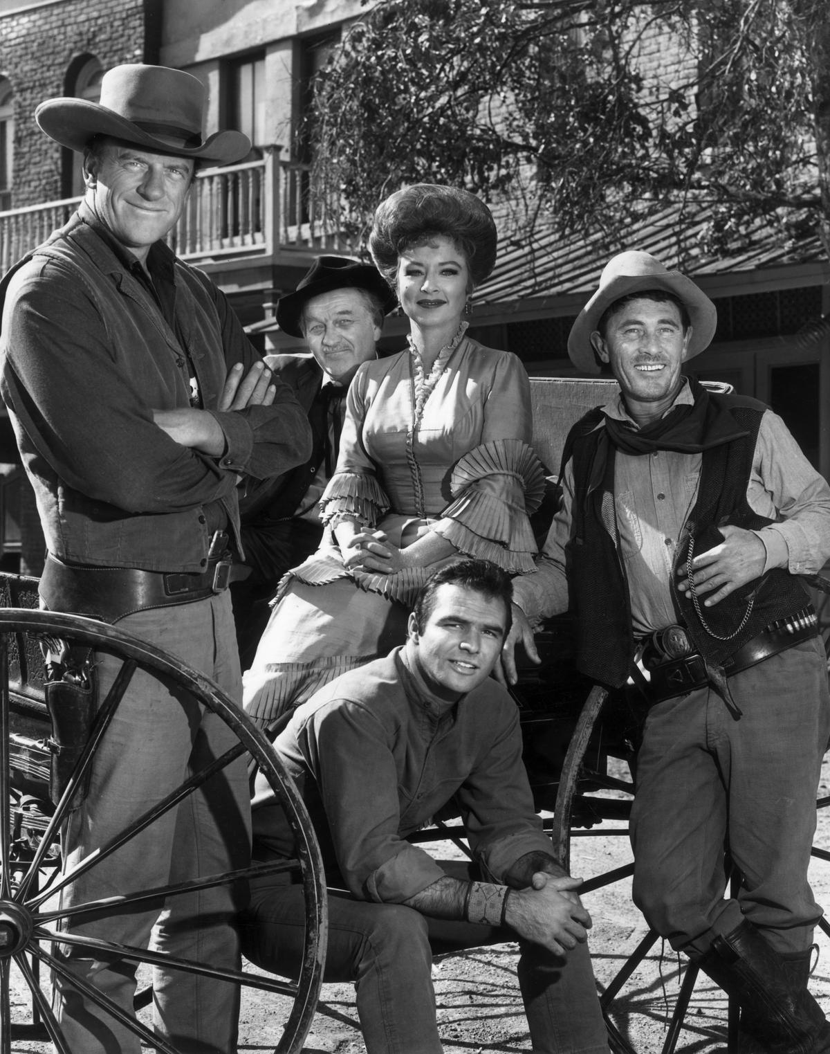 The "Gunsmoke" cast (L–R) James Arness, Milburn Stone, Amanda Blake, Burt Reynolds (seated), and Ken Curtis pose around a wagon in a promotional portrait for the Western television series. (Hulton Archive/Getty Images)