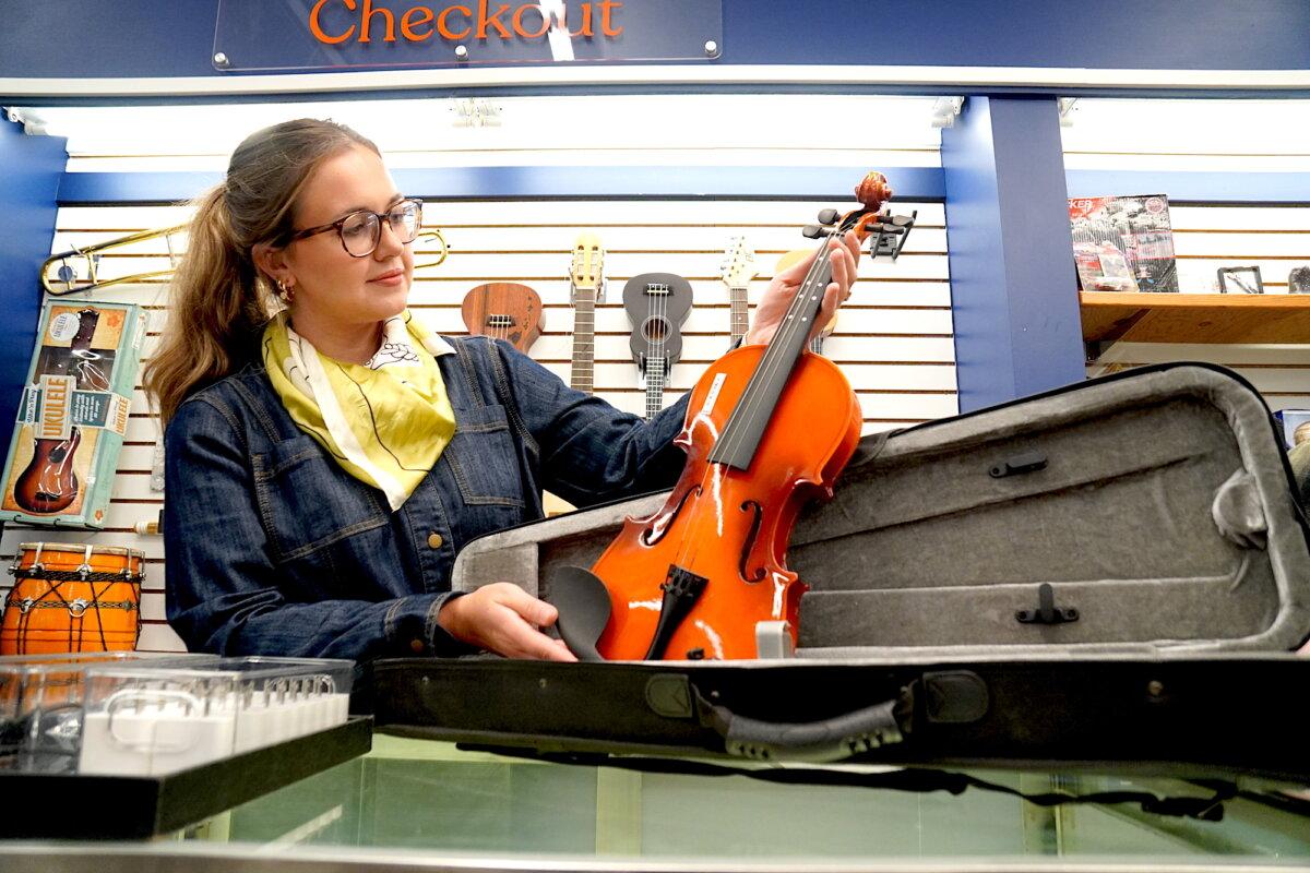 Unclaimed Baggage Senior Public Relations Director Sonni Hood examines a violin in pristine condition on Oct. 8, 2025. (Allan Stein/The Epoch Times)