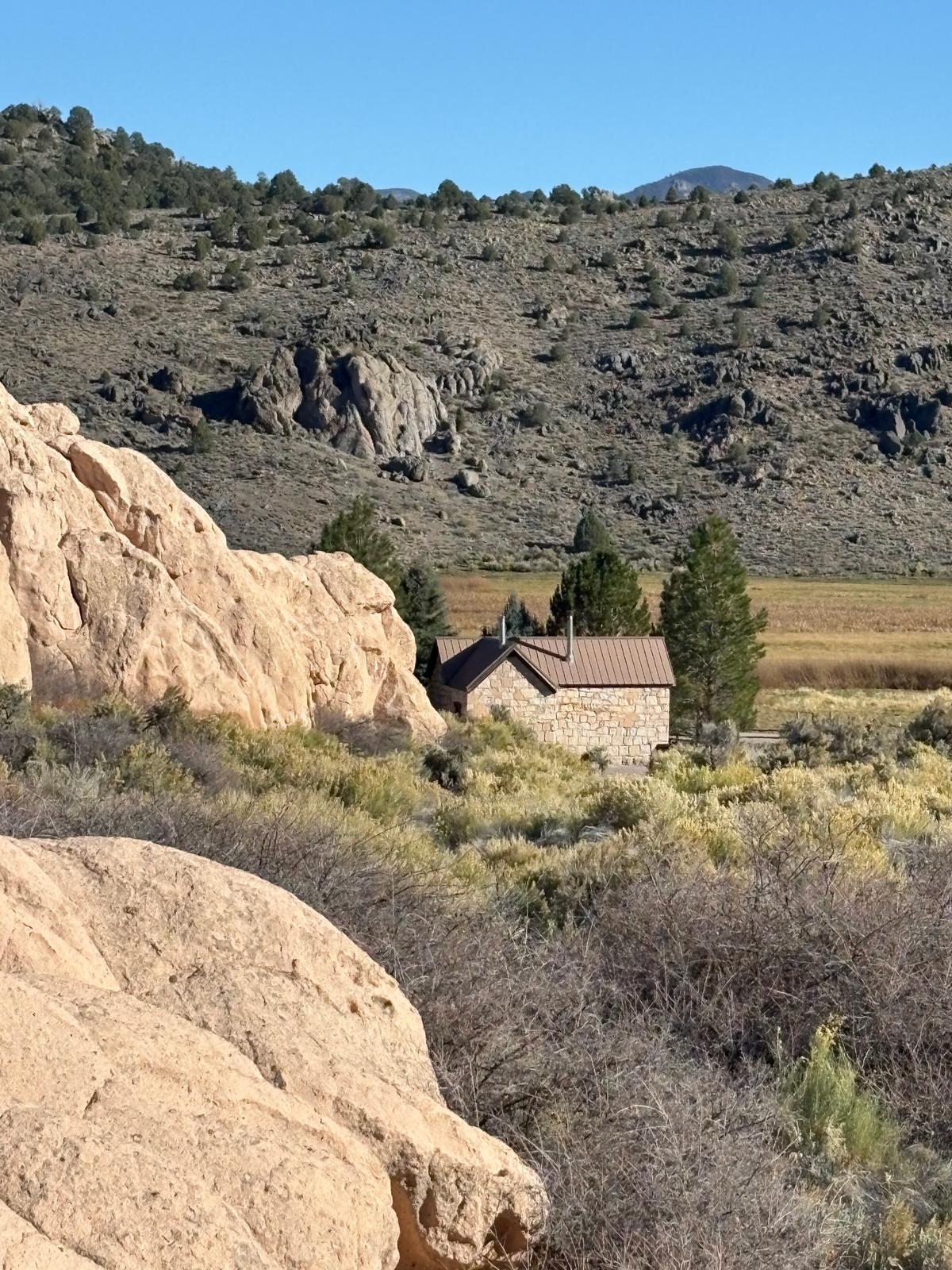 The Moody Stone Cabin cuts a diminutive figure against the massive rocky bluffs of Lincoln County, Nev. (Deena Bouknight)
