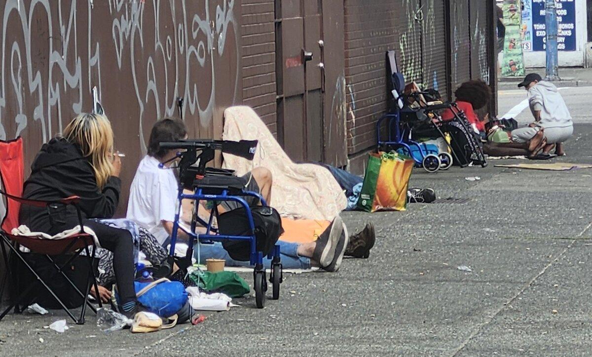 Individuals sit on the sidewalk in Vancouver's Downtown Eastside on Aug. 28, 2025. (Paul Rowan Brian/The Epoch Times)