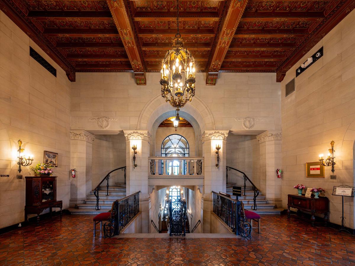 A grand marble, double staircase ascends from the entrance hall to the second-floor loggia and descends to the first-floor gallery. The house had 861 light bulbs illuminating the interior, many in fixtures such as this exquisite bronze chandelier. The walls are constructed of limestone, and a large Palladian arch frames the stairs. The wrought iron seen throughout the interior is a common feature of Tuscan architecture. (Kit Leong/Shutterstock)