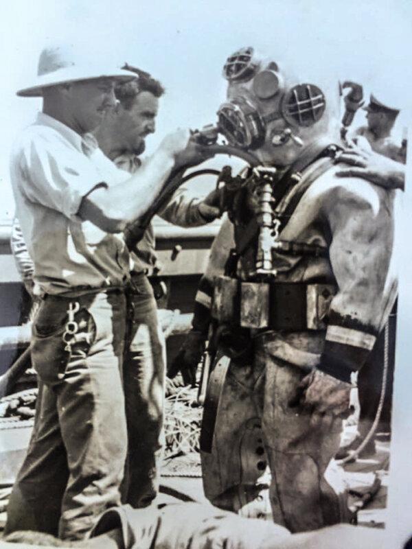 Ken Hartle (2nd left) assisting another diver suiting up. (Public Domain)
