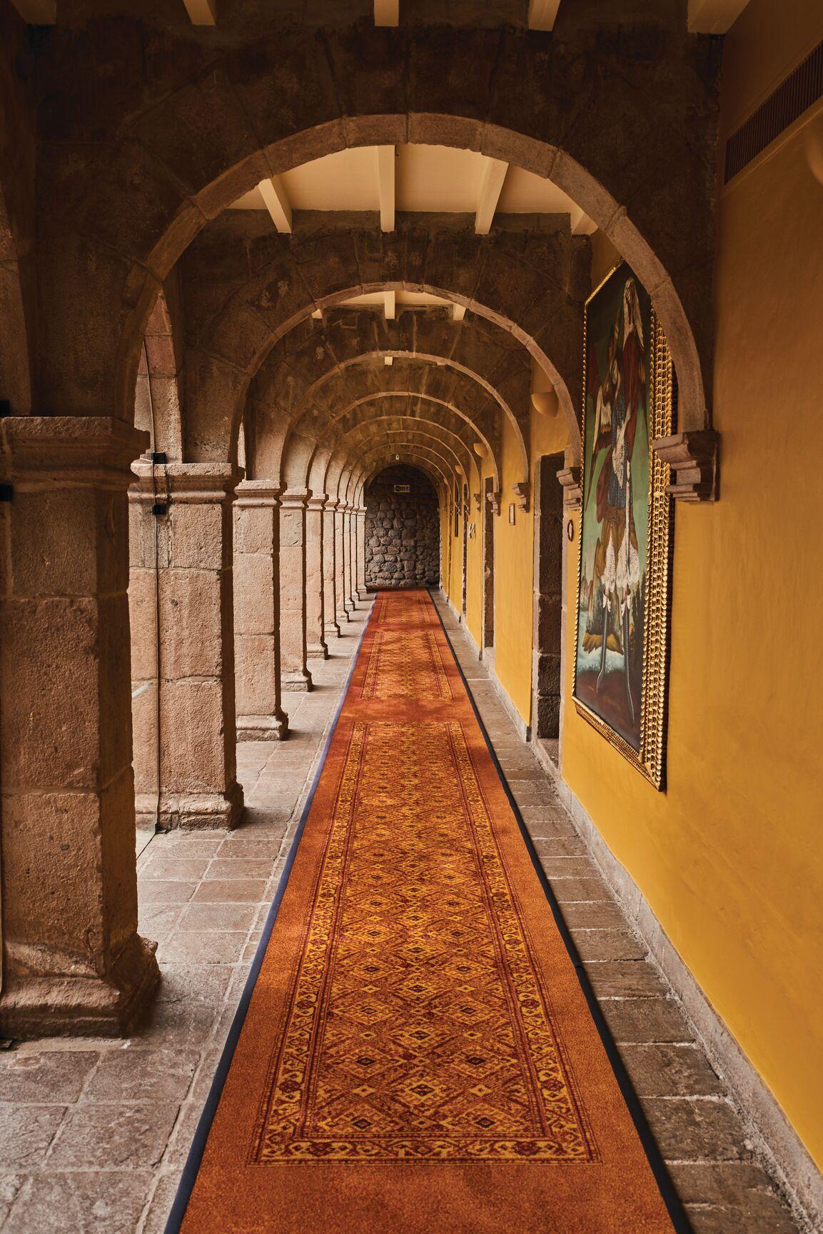 The elongated, arched arcades, also referred to in a monastery or seminary as cloisters, symmetrically frame the rectangular courtyard. These covered stone pathways, supported by stone-block columns, feature gold-painted walls hung with 18th-century colonial Cusquenian (Cusco school) oil paintings. (Javier Falcón/Belmond)