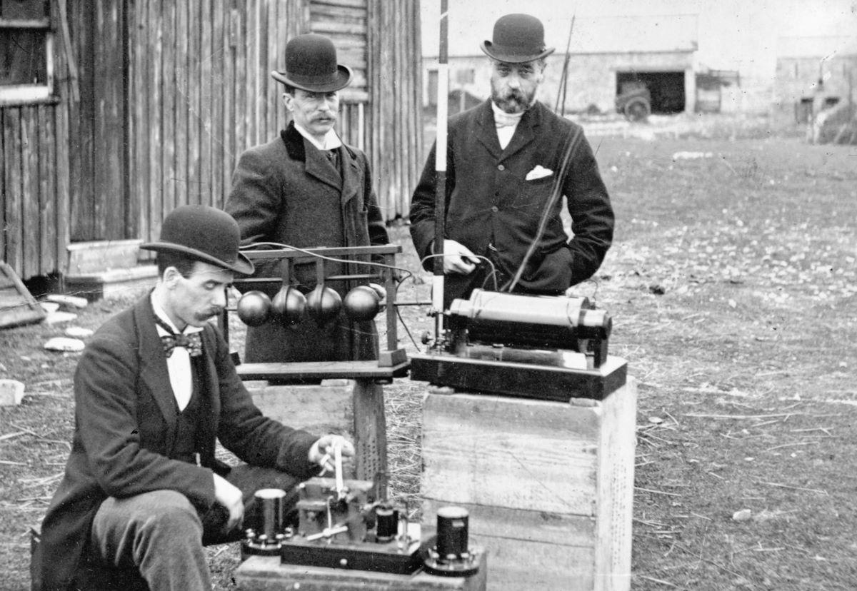 British Post Office engineers inspect Marconi's radio equipment during a demonstration on Flat Holm Island in the Bristol Channel, May 1897. The transmitter is at the center, the receiver below it, and the pole supporting the wire antenna is visible at top. (<a href="https://commons.wikimedia.org/wiki/User:Materialscientist">Materialscientist</a>/<a href="https://creativecommons.org/licenses/by/3.0/">CC BY 3.0</a>)