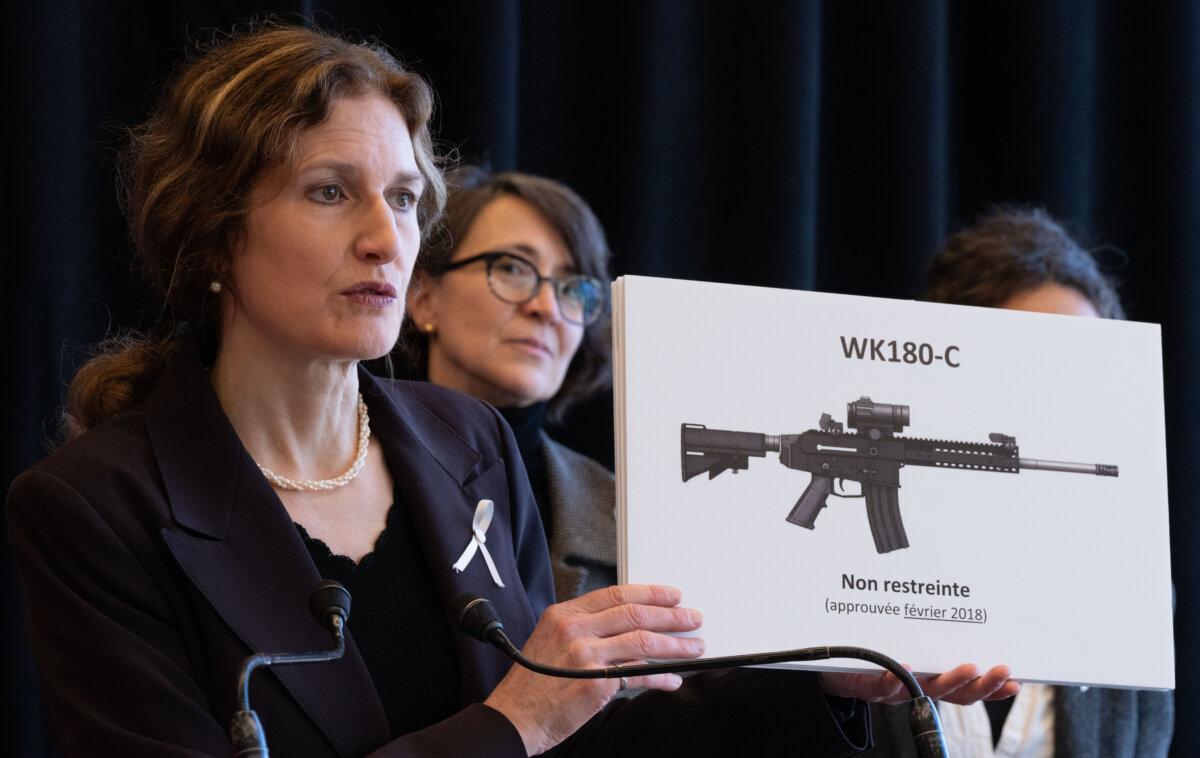 Heidi Rathjen, coordinator of PolySeSouvient, holds a sign showing a gun still legal in Canada as Nathalie Provost, spokesperson and survivor of the 1989 massacre at Ecole Polytechnique, looks on during a press conference about stricter gun control in Montreal on Nov. 19, 2024. (The Canadian Press/Christinne Muschi)