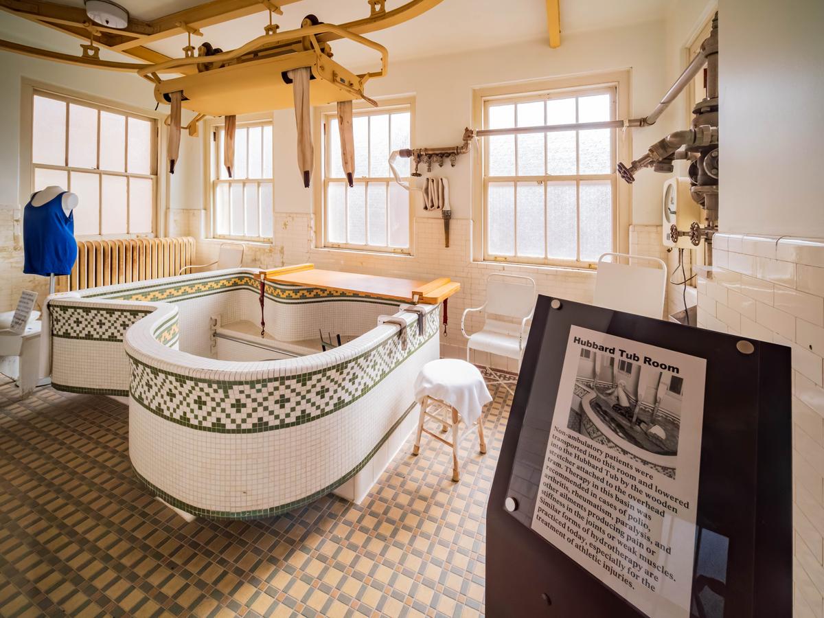 The Hubbard Tub room includes a deep, therapeutic bathtub. Designed by engineer Carl Hubbard, the tub was constructed with tiles by the Mosaic Tile Co. of Ohio. The olive green tile pattern in the tub is accentuated by a complementary floor tile pattern. Overhead in this utilitarian room at Fordyce is an electric hoist for assisting individuals who once enjoyed a soak in the large, embellished bathtub. (Kit Leong/Shutterstock)