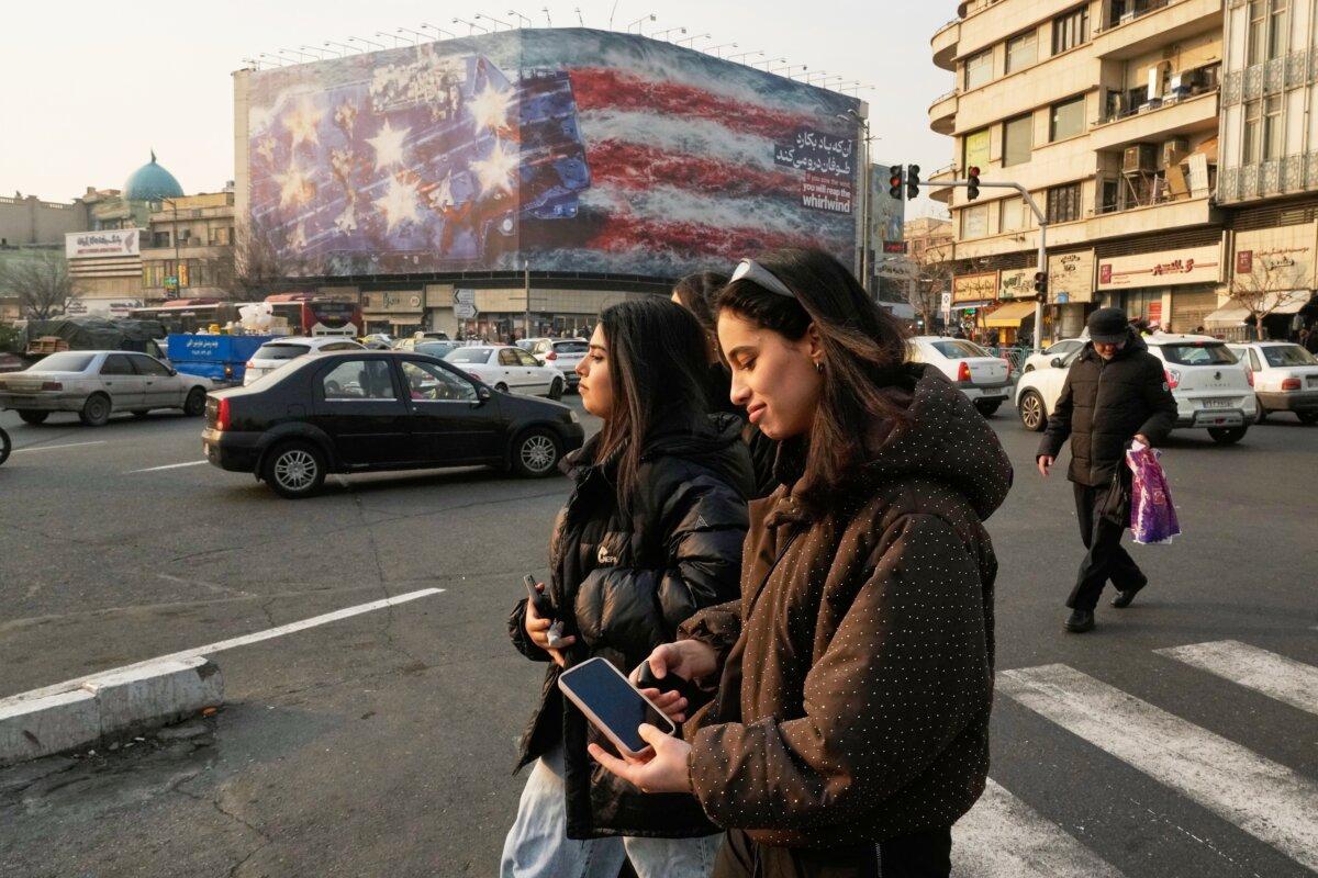 People walk past a billboard depicting a damaged U.S. aircraft carrier with the slogan 'If you sow the wind, you'll reap the whirlwind,' at Enqelab-e-Eslami (Islamic Revolution) Square in Tehran, Iran, on Jan. 25, 2026. (Vahid Salemi/AP)