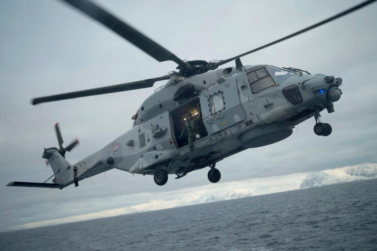 A French sailor is seen at the door of a helicopter as it takes off from the French navy frigate Normandie during a patrol in a Norwegian fjord, north of the Arctic circle, on March 7, 2024. (AP Photo/Thibault Camus)