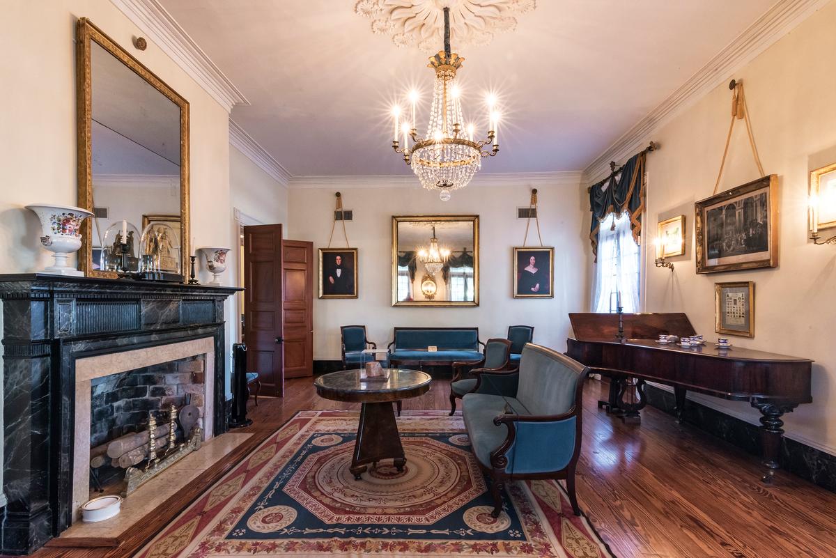 Paneled doors made of cypress wood open from the mansion’s entryway into the parlor. Hanging from a large, decorative medallion on the parlor’s ceiling is an exquisite focal point: a crystal-and-brass chandelier with a circular candelabra. Polished heart pine covers the floors, while the mantel is painted to look like black-and-white marble. Blue velvet-covered French Charles X and Louis Philippe style furnishings provide seating in this room. (Oak Alley Foundation)